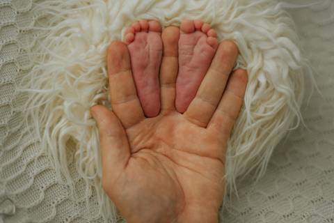 detalhe dos pés do bebê na mão do pai em ensaio newborn de recém-nascido'