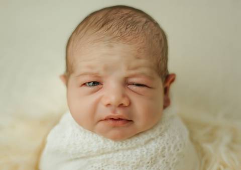 foto de bebê piscando com um olho só em ensaio newborn de recém-nascido'