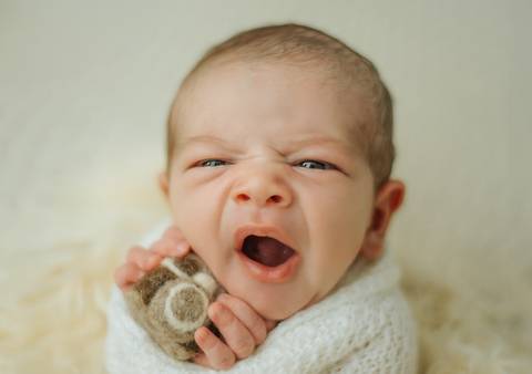bebê bocejando e segurando uma camera de brinquedo em ensaio newborn de recém-nascido'