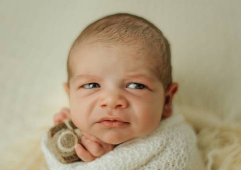 bebê olhando para o lado segurando camera fotográfica em ensaio newborn de recém-nascido'