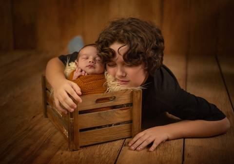 irmão abraçando bebê em ensaio newborn de recém-nascido'