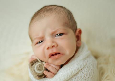 bebê sério segurando câmera de feltragem em ensaio newborn de recém-nascido'