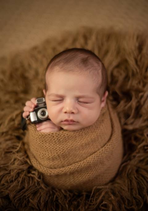 bebê segurando câmera fotográfica em ensaio newborn de recém-nascido'