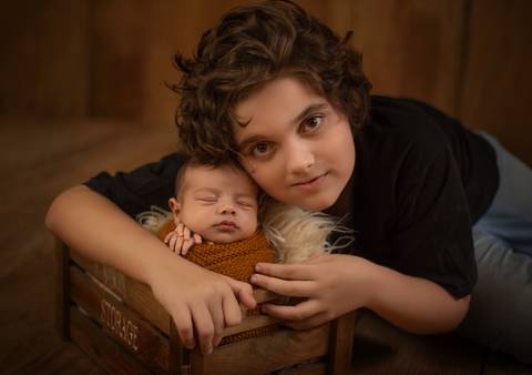 menino olhando para câmera em ensaio newborn com irmão em ensaio newborn de recém-nascido'