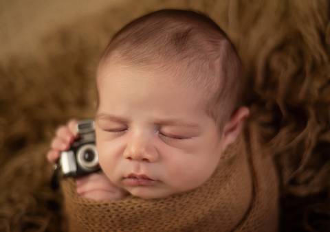 bebê de ladinho segurando câmera em ensaio newborn de recém-nascido'