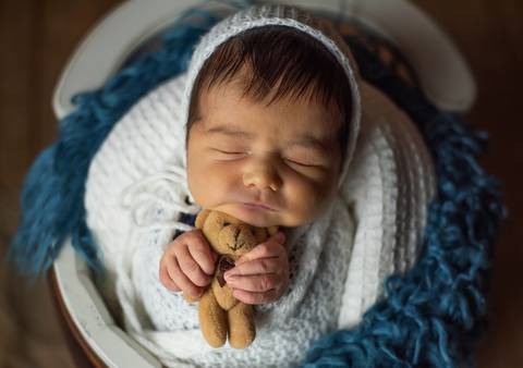 bebê enrolado dentro do cestinho segurando ursinho'