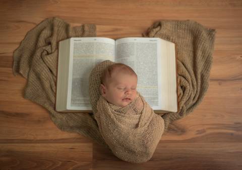 bebê enroladinho deitado sobre bíblia em cima de tecido em formato de coração'