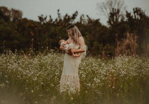 mulher amamentando bebê em campo de flores'