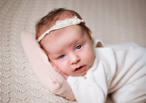 Expressão serena de recém-nascido em pose natural no ensaio.'