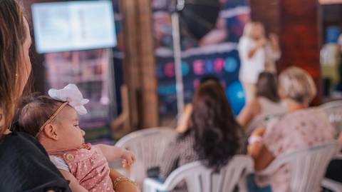 Olhar expressivo de bebê no colo de Aline Fontes durante o ensaio ao vivo.'