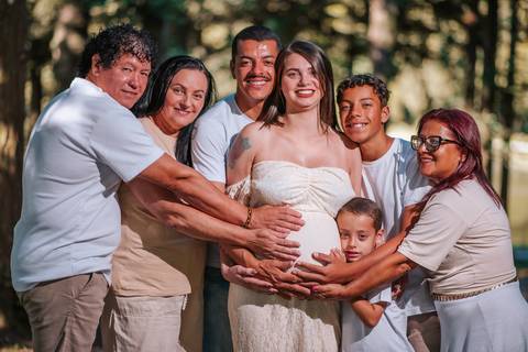 Ensaio de família com gestante no gramado do Parque dos Pinheiros, Farroupilha: pais e filhos brincando sob a sombra das árvores centenárias'