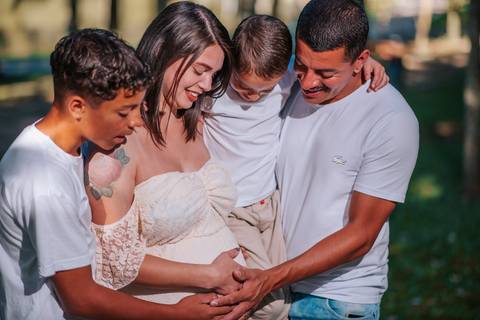 Ensaio gestante lifestyle no Parque dos Pinheiros, Farroupilha: casal grávido compartilhando risadas no banco de madeira às margens do lago'