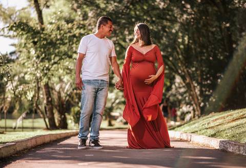 Ensaio gestante em estilo documental no Parque dos Pinheiros, Farroupilha: grávida refletindo serenidade sob a copa das árvores, com paisagem urbana ao fundo'
