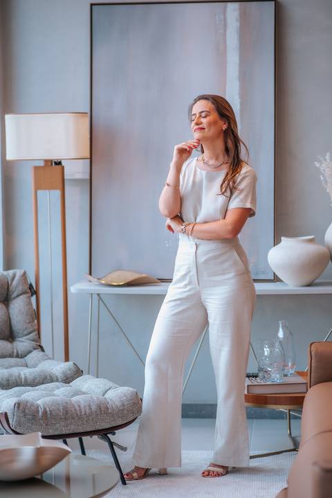 Mulher em pé com pose introspectiva, usando look neutro em espaço de decoração sofisticado.

'