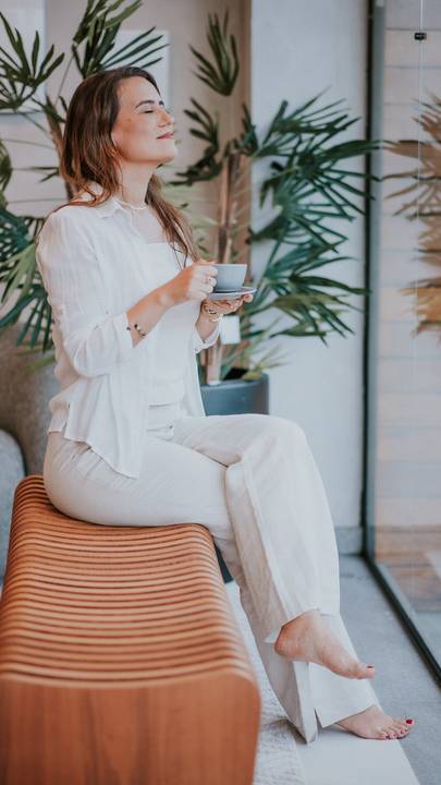 Foto de corpo inteiro de mulher elegante em ambiente decorado com tons suaves.

'