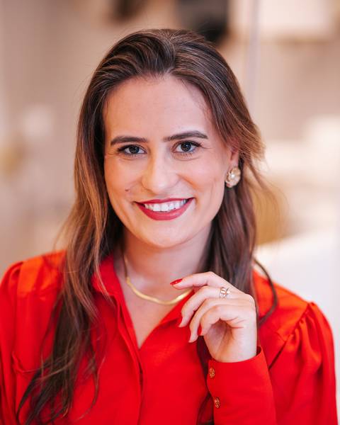 Mulher sorrindo com expressão confiante, usando camisa vermelha em ambiente elegante.'