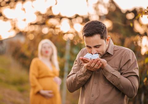 Mãe acariciando a barriga com terço e sapatinhos de bebê. Ensaio que une fé, maternidade e emoção.'