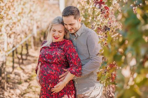 Casal sorrindo juntos, entre folhas secas e vinhas, retratando a espera por uma nova fase da vida.'
