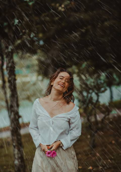 Imagem de mulher abraçando a si mesma na chuva, representando acolhimento e conexão interior.'