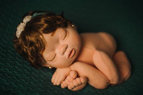 Boneca reborn Jolie com tiara e mãos cruzadas, em pose típica de ensaio newborn, simulando prática segura para fotógrafos iniciantes.'