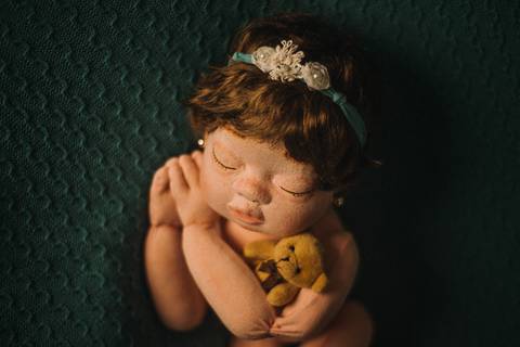 Boneca de transição posicionada em pose lateral com tecido e composição estilo newborn, utilizada em treinamento para fotografia neonatal.'