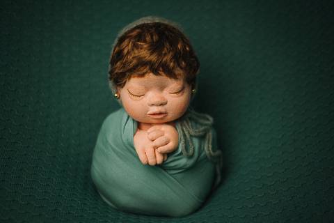 Boneca reborn segurando ursinho, deitada com expressão serena, representando estudo de composição em fotografia newborn realista.'