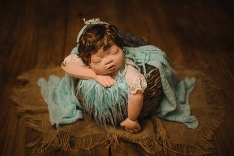 Close da boneca reborn segurando ursinho, com wrap verde, aplicada em mentorias sobre direção de cena e afeto em fotografia newborn.'