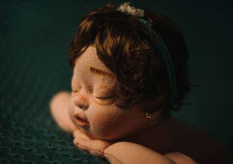 Close lateral da boneca reborn com tiara e fundo escuro, ideal para estudo de foco, iluminação suave e prática de retrato newborn.'