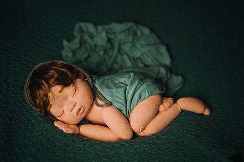 Boneca de transição posicionada em pose lateral com tecido e composição estilo newborn, utilizada em treinamento para fotografia neonatal.'