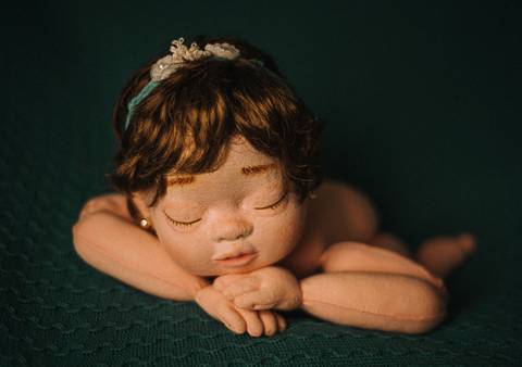 Boneca reborn posicionada com braços cruzados sob o queixo, pose tradicional usada em sessões de newborn real para ensinar técnica e iluminação.'