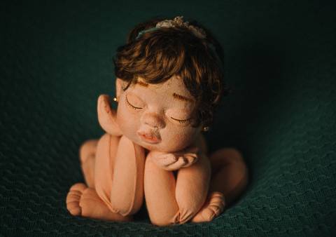 Boneca reborn com manta escura simulando apoio, em pose sentada fisiológica usada como modelo para prática de ensaios newborn.'