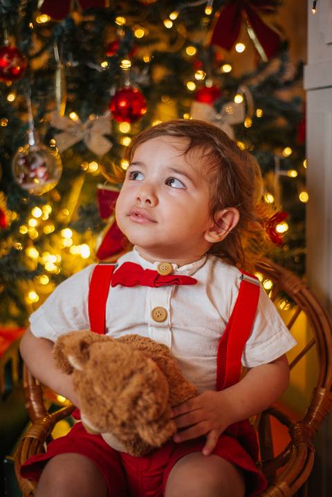 Criança sorrindo em cenário de Natal com neve artificial.'