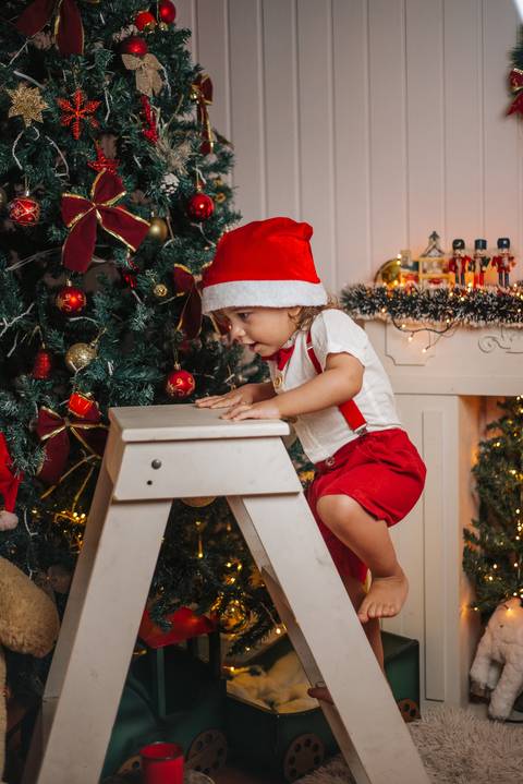 Bebê em mini-cama natalina com elementos vermelhos e dourados.'