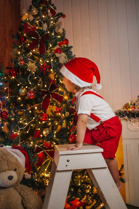 Criança abrindo presente em cenário de Natal iluminado.'