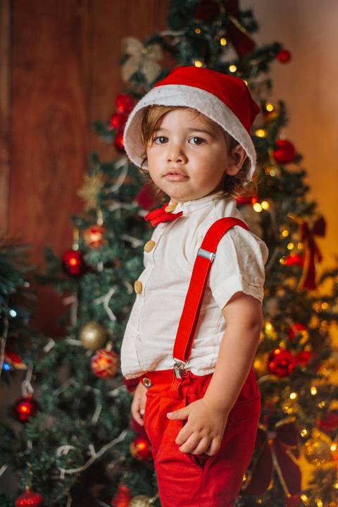 Foto de bebê com luzes natalinas desfocadas ao fundo.'