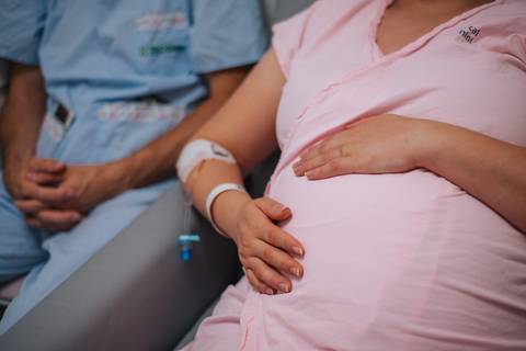 Gestante em pré-parto no Hospital Tacchini com mãos apoiadas sobre a barriga, fotografia de parto em Bento Gonçalves.'