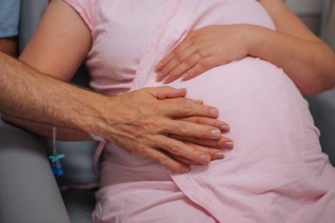 Detalhe das mãos do casal sobre a barriga da gestante em ambiente hospitalar, ensaio de parto humanizado em Bento Gonçalves.'