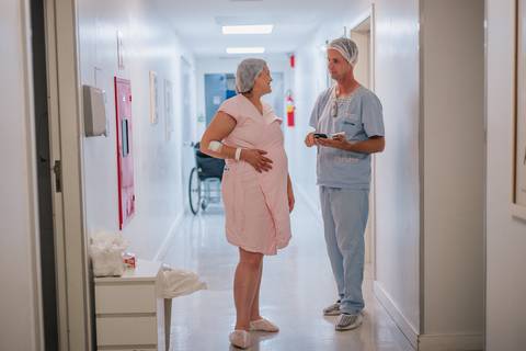 Gestante caminhando no corredor do Hospital Tacchini acompanhada do parceiro antes da cesariana, fotografia documental de parto.'