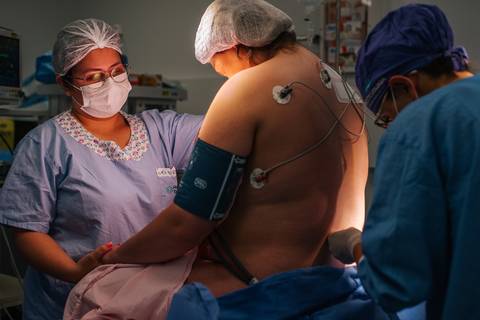 Gestante sentada para anestesia durante cesariana no Hospital Tacchini, fotografia de parto hospitalar em Bento Gonçalves.'