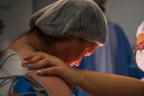 Momento de apoio e acolhimento durante o parto cesariana no Hospital Tacchini, fotografia de parto com foco emocional.'