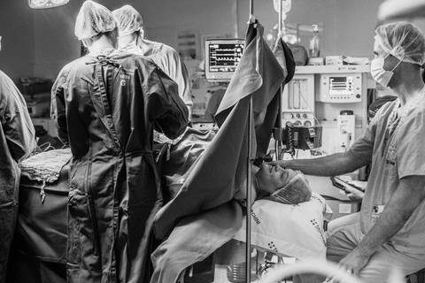 Equipe médica durante parto cesariana no Hospital Tacchini, cobertura fotográfica de nascimento hospitalar.'