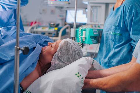 Mãe aguardando o nascimento da filha na sala cirúrgica do Hospital Tacchini, fotografia documental de parto.'