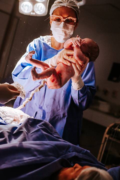 Bebê sendo apresentado à mãe logo após o nascimento, cobertura fotográfica de parto hospitalar.'