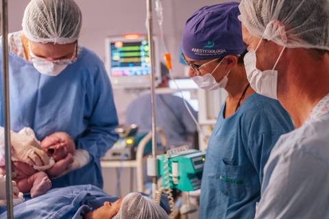 Equipe médica realizando os primeiros cuidados com a recém-nascida, fotografia de parto hospitalar.'