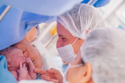 Primeiro contato entre mãe e bebê após o nascimento durante cesariana no Hospital Tacchini, fotografia de parto.'