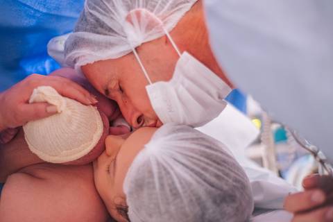 Mãe beijando a bebê logo após o nascimento na sala cirúrgica, fotografia de parto emocional em Bento Gonçalves.'