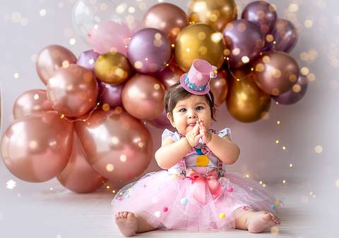 Bebê sentada em ensaio Smash the Cake em estúdio, usando vestido em tons suaves e cenário com balões, ensaio de 1 ano em Farroupilha.'
