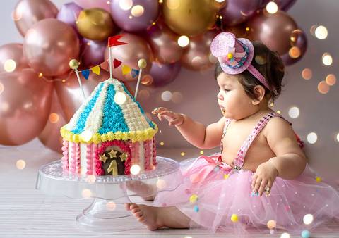 Bebê em ensaio Smash the Cake sentada ao lado do bolo decorado, cenário temático e composição pensada para aniversário de 1 ano.'