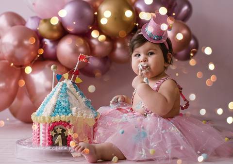 Bebê sentada em ensaio Smash the Cake explorando o bolo decorado, cenário personalizado e iluminação suave.'