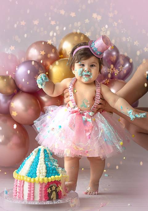Ensaio Smash the Cake com bebê interagindo com o bolo, vestido delicado e cenário personalizado para aniversário de 1 ano.'
